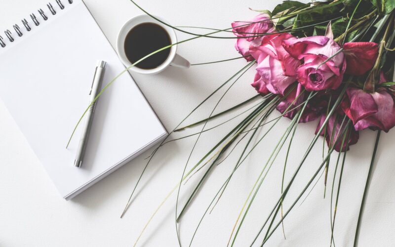 red rose flowers bouquet on white surface beside spring book with click pen and cup of cofffee